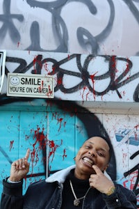 a man in a black jacket standing in front of a graffiti covered wall